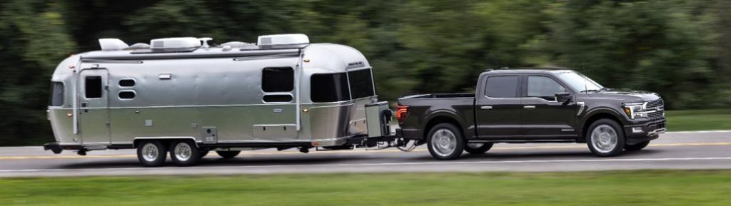 Ford F Series Towing a Camper Driving on a Forest Road Side View