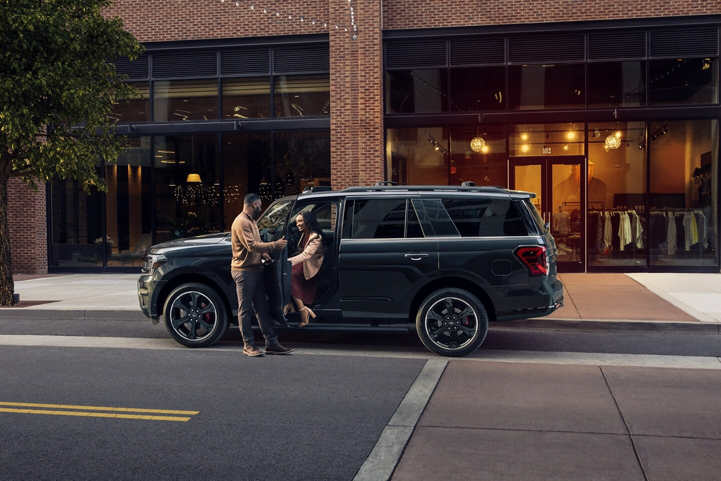 Man Helping a Woman out of a Ford Expedition Parked Side View Next to a City Curb